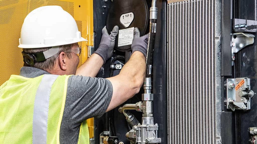 Een arbeider in veiligheidsuitrusting inspecteert machines met pijpen en componenten in de buurt van een grote radiator.