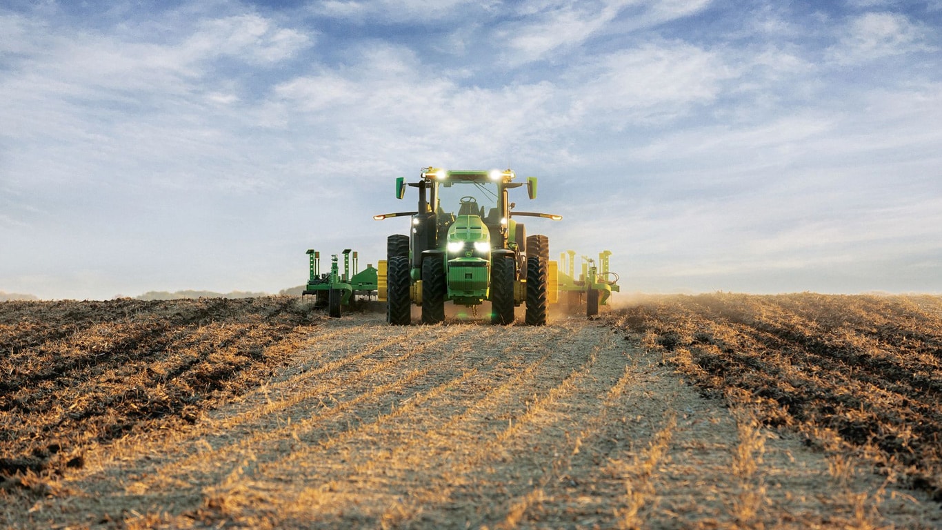 Zelfrijdende John Deere tractor trekt grondbewerkingsmachines door een open veld.