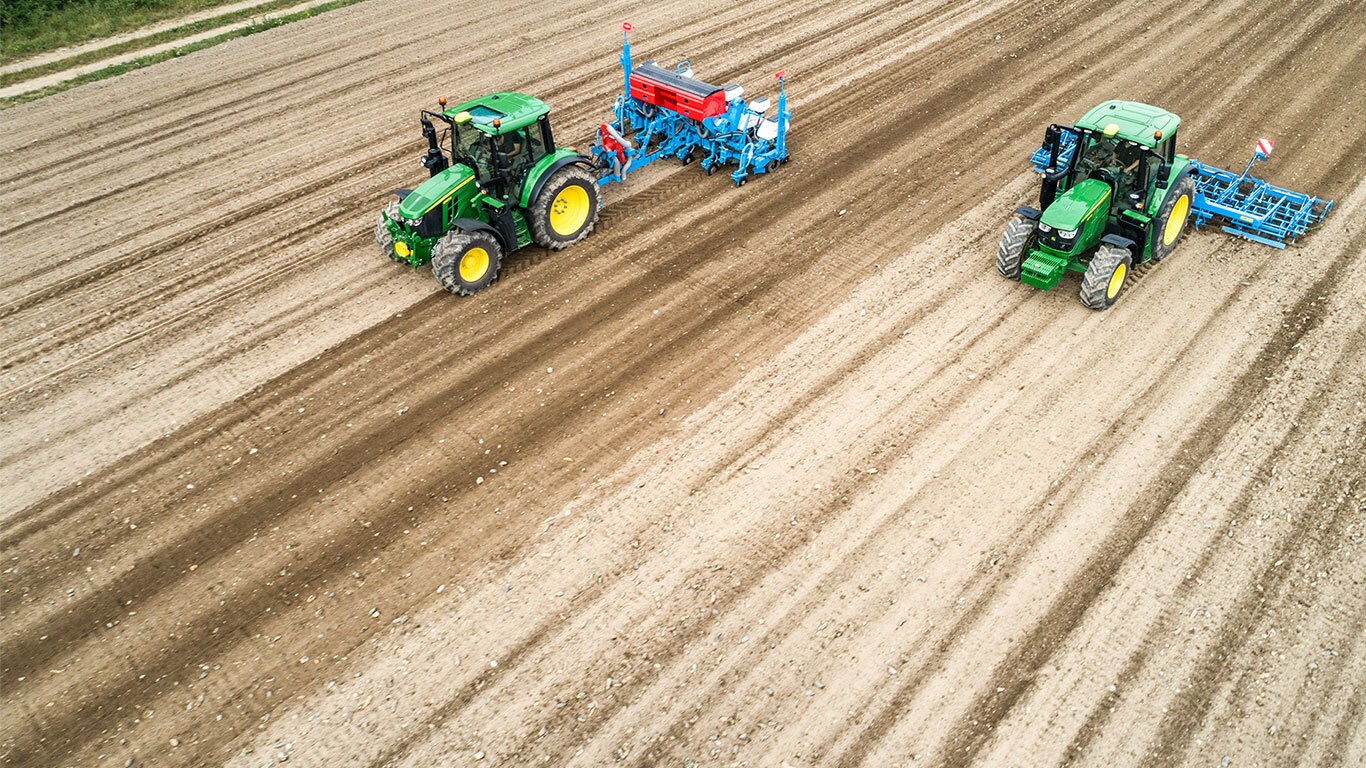 Twee John Deere 6M-tractoren op een braakliggend veld De ene trekt een Monsomen-zaaimachine. De andere trekt een Lemken-zaaibedcombinatie