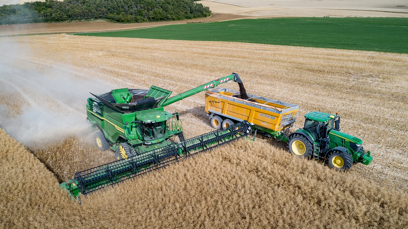 John Deere X-Series maaidorser die raapzaad lost in een graanwagen getrokken door een John Deere tractor