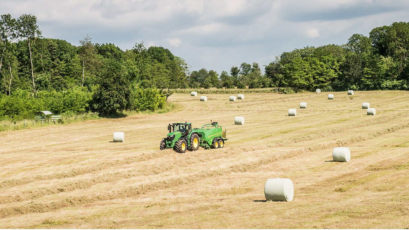 John Deere tractor met balenpers in veld met kuilvoerbalen