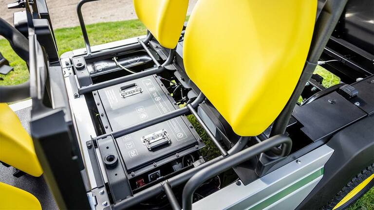 Close-up van twee lithium-accupakketten gemonteerd onder felgele stoelen in een John Deere Gator GS elektrisch universeel voertuig.