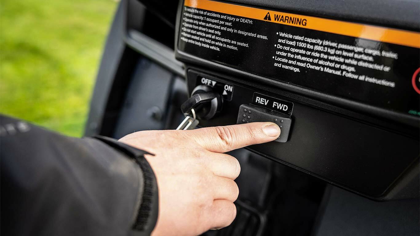 Vinger die drukt op de knop voor vooruitversnelling op het bedieningspaneel van een John Deere Gator GS elektrisch model.