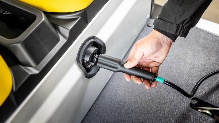Hand die oplaadkabel in de zijaansluiting steekt van een John Deere Gator GS elektrisch universeel voertuig.