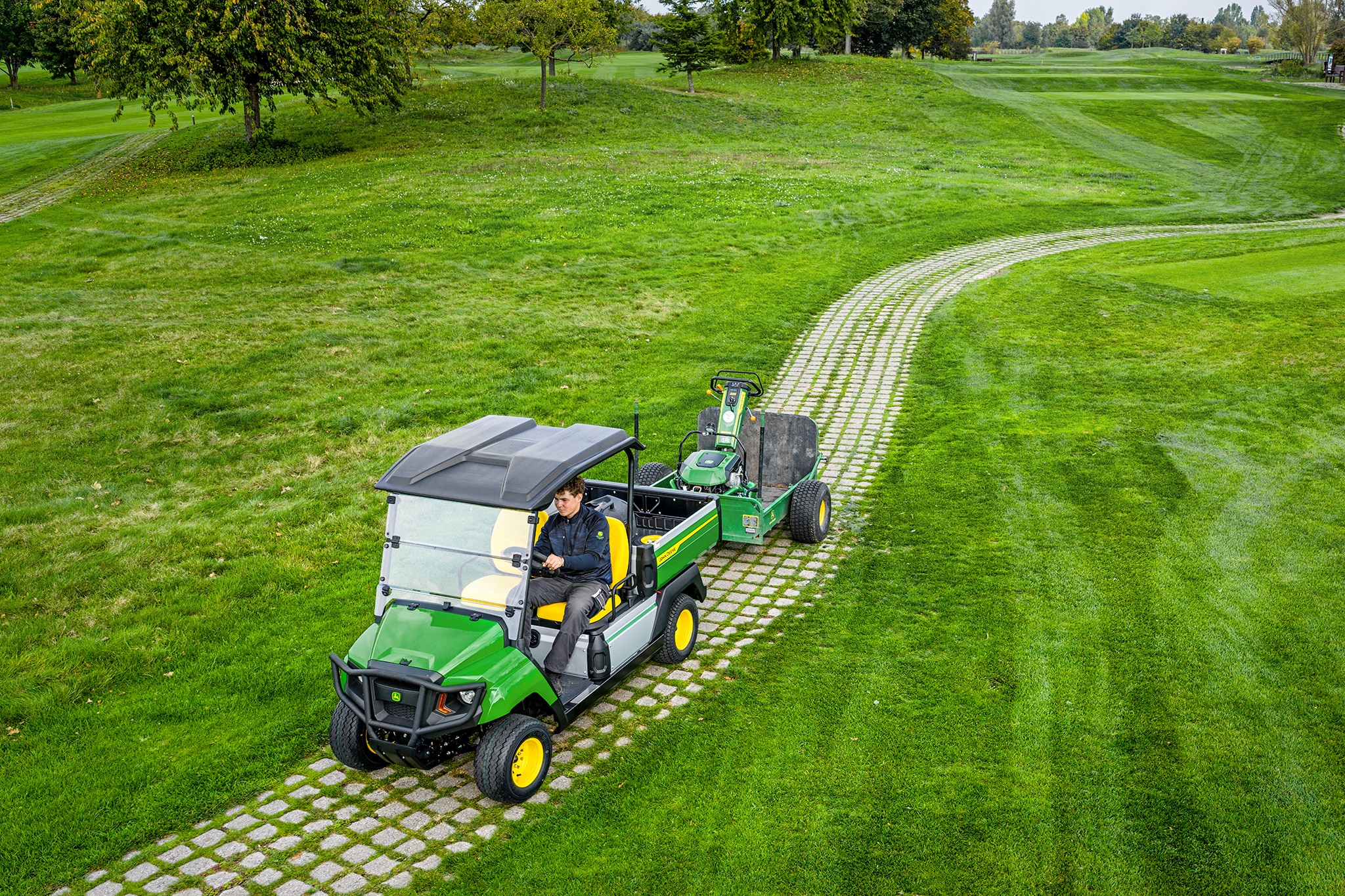 John Deere Gator GS die apparatuur sleept op een grasachtig golfbaanpad
