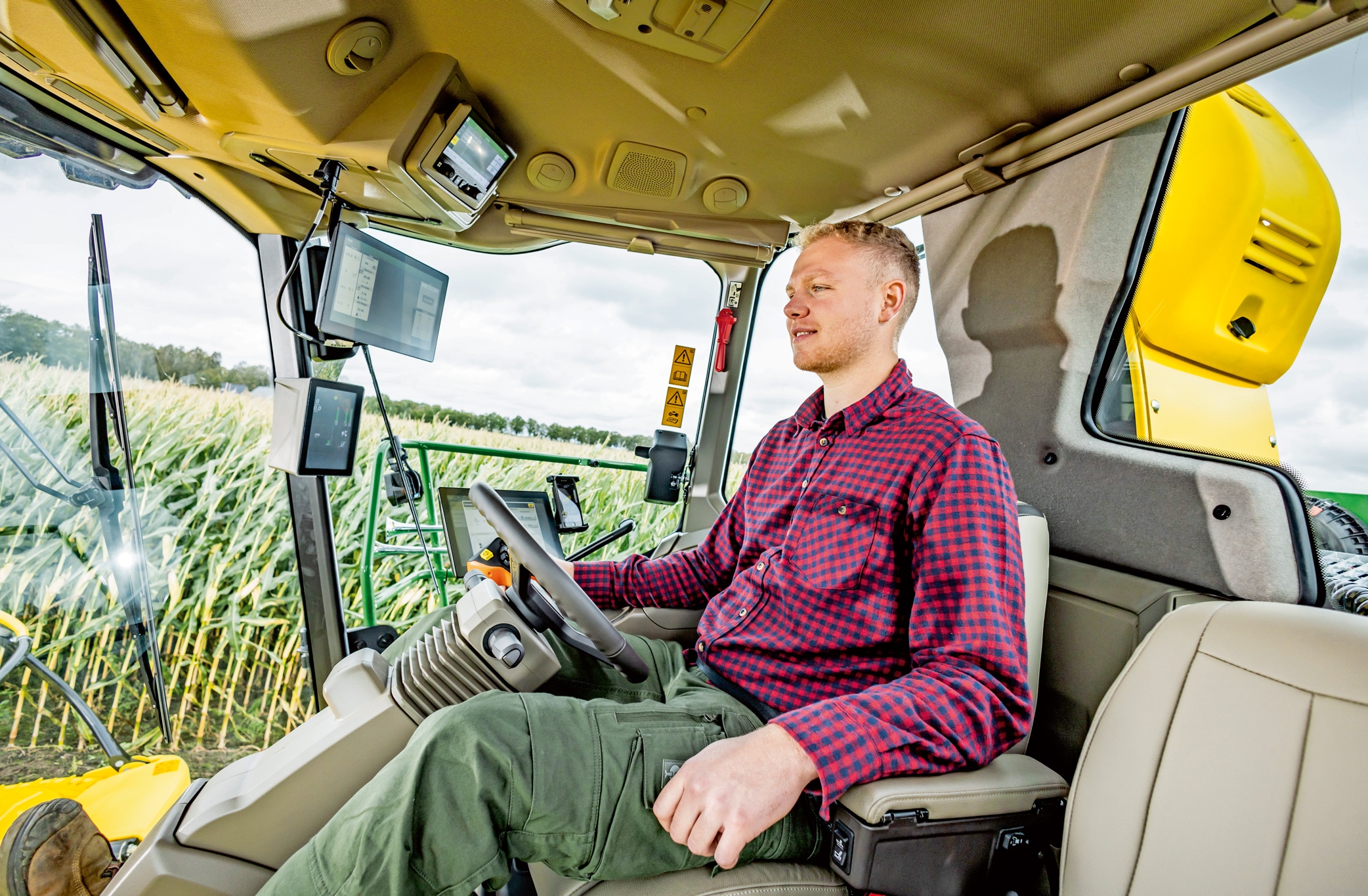 Een landbouwer die een moderne landbouwmachine bedient in een maisveld, met geavanceerde technologie en uitrusting vanuit de tractorcabine.