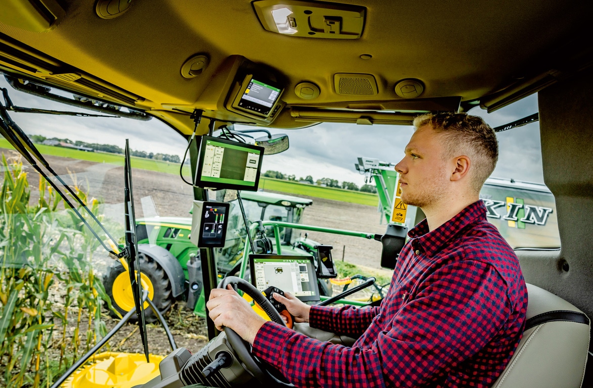 Een boer die een geavanceerde landbouwmachine met meerdere digitale schermen in een cabine van een zelfrijdende veldhakselaar bedient: een demonstratie van moderne landbouwtechnologie in een veld.