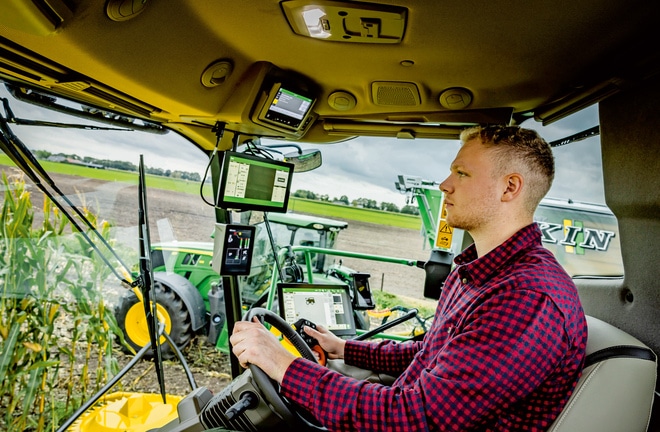 Een boer die een geavanceerde landbouwmachine met meerdere digitale schermen in een cabine van een zelfrijdende veldhakselaar bedient: een demonstratie van moderne landbouwtechnologie in een veld.