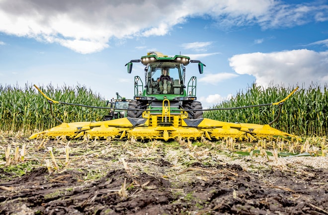 Moderne landbouwmachines die mais oogsten in een veld onder een deels bewolkte lucht: een demonstratie van geavanceerde landbouwtechnologie en -uitrusting.