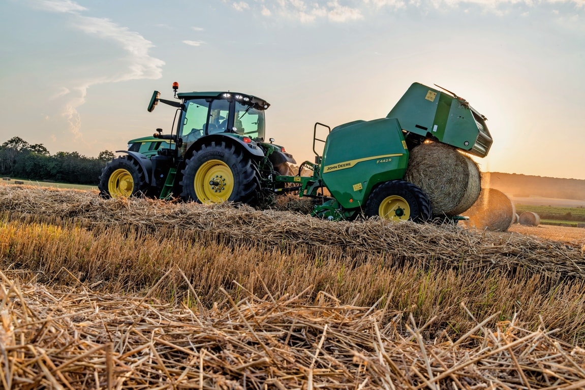 John Deere F442M-balenpers getrokken door een John Deere 6M-tractor die een strobaal uitwerpt