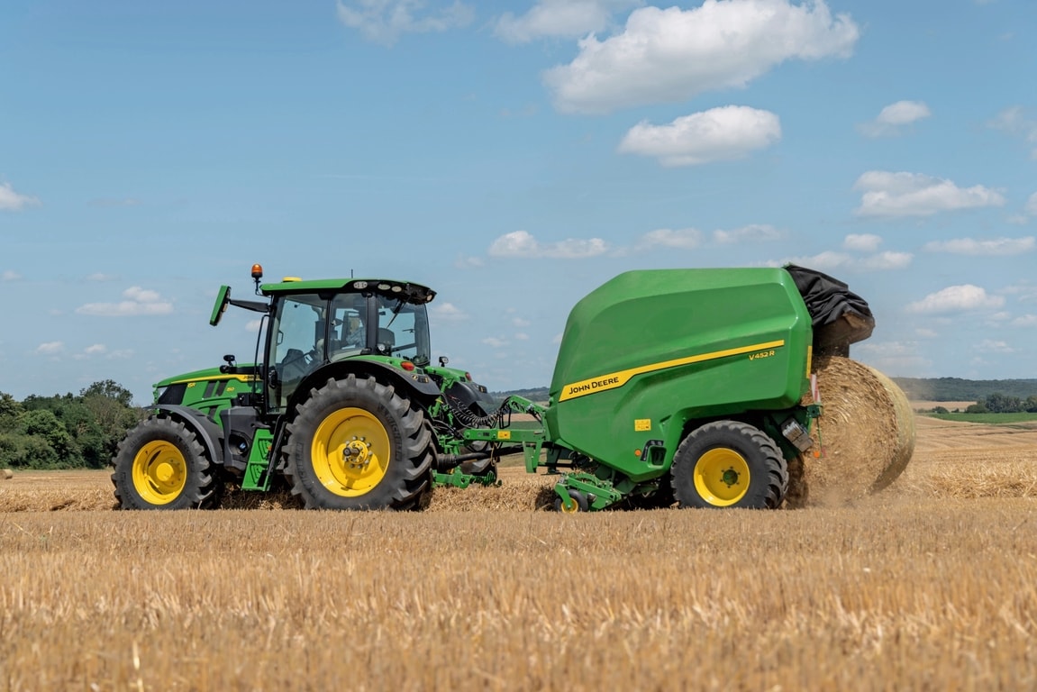 John Deere V452R op een stroveld getrokken door een John Deere 6R 150 die een baal uitwerpt