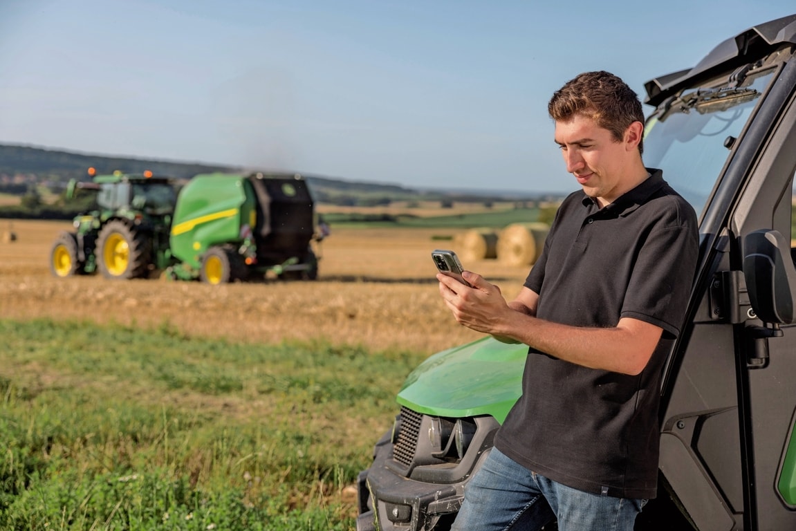 Persoon die de baaldocumentatiegegevens op de mobiele telefoon controleert met een John Deere VR-balenpers op de achtergrond