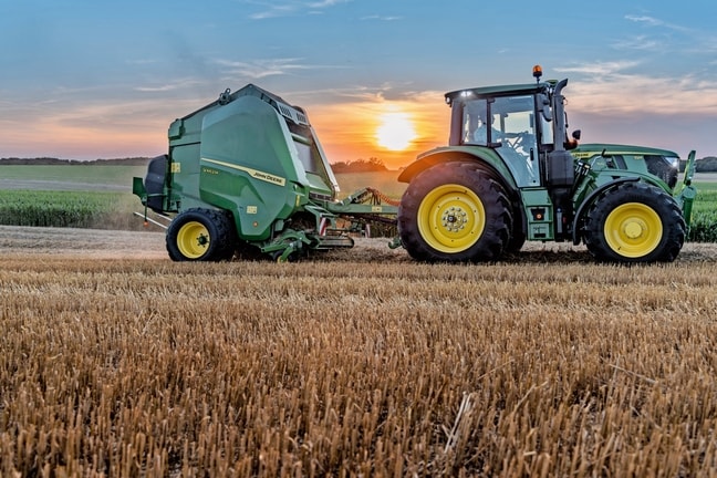 John Deere V462M op een stroveld getrokken door een John Deere 6M 150 bij zonsondergang