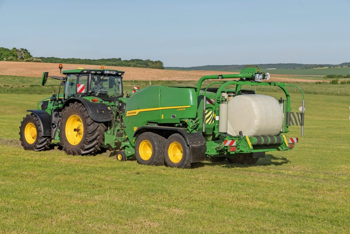 John Deere C442R-pers-wikkelcombinatie getrokken door een John Deere 6R 185 die kuilvoerbalen met hoge dichtheid maakt
