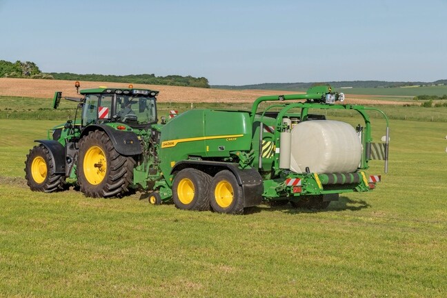 John Deere C442R-pers-wikkelcombinatie getrokken door een John Deere 6R 185 die kuilvoerbalen met hoge dichtheid maakt