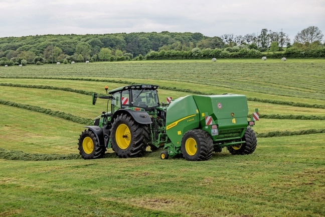 John Deere F442R-balenpers getrokken door een John Deere 6M-tractor op een heuvelachtig grasveld