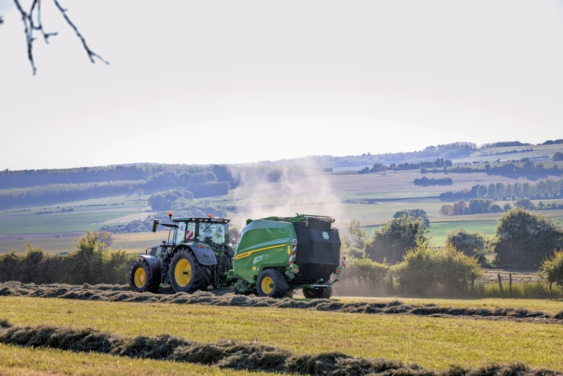 John Deere V462R getrokken door een John Deere 6R 185-tractor die hooibalen maakt