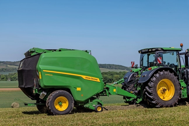 John Deere V462R getrokken door een John Deere 6R 185-tractor die hooibalen maakt